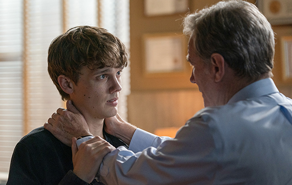 An older man places his hands on the neck and shoulders of a young man while looking at him.