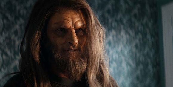 A person with long brown hair and deeply textured, weathered skin looking slightly to the side.