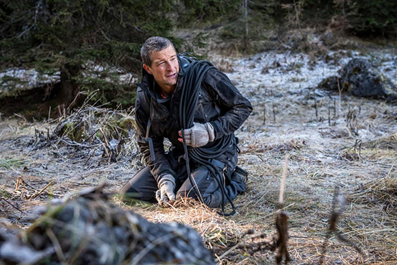 A man in dark clothing kneels in a frosty field while holding a thick black rope.