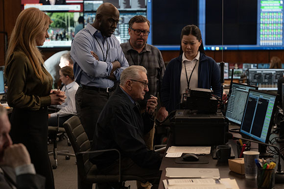 A group of diverse professionals looking at computer monitors in a dimly lit command center.