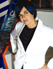 A person with dark hair and blue highlights wearing a white blazer and black shirt.
