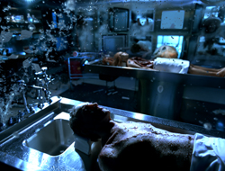 A person lies on a metal examination table while water splashes around them in a dark, clinical room.