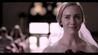 A woman with blonde hair pulled back wears a white veil and smiles slightly.