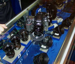 Nikon camera and various lenses displayed on blue stands inside a glass case.