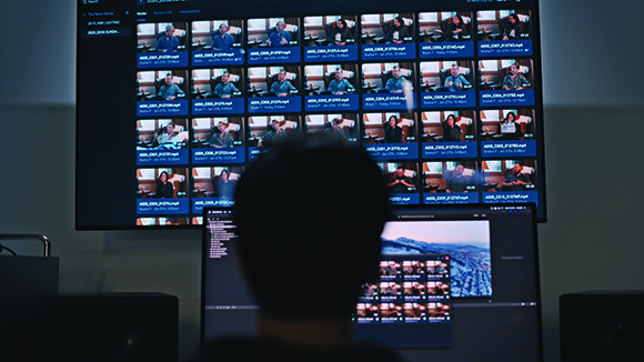 A person's silhouette looking at a large screen displaying a grid of multiple video call windows.