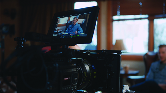 A close-up view of a professional cinema camera monitor displaying a man being interviewed.