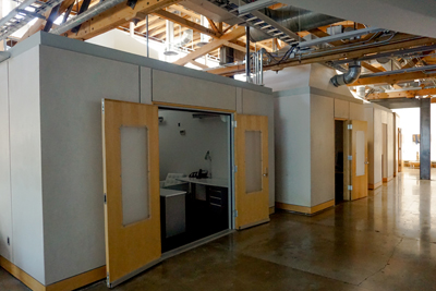 Modular grey office pods with light wood doors stand under an exposed wooden ceiling structure.