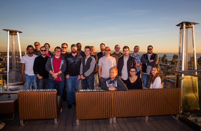 A large group of diverse people standing together on a rooftop terrace during sunset.