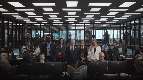 A group of professionals standing behind desks in a large, glass-walled office space.