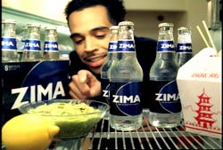 A man points toward several glass bottles of Zima labeled with blue and white branding near food.