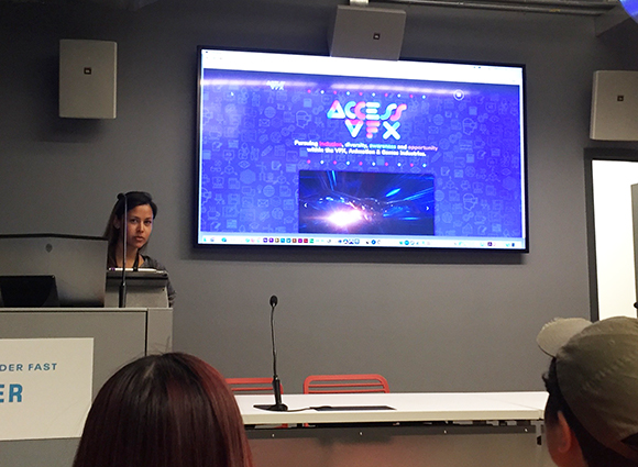 A woman stands behind a podium with a laptop, looking towards a large screen displaying the Access VFX logo and text about pu