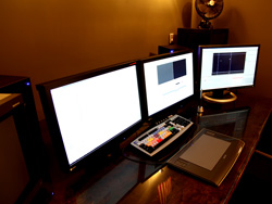 Three computer monitors side-by-side on a desk with a control panel and a digital tablet in the foreground.