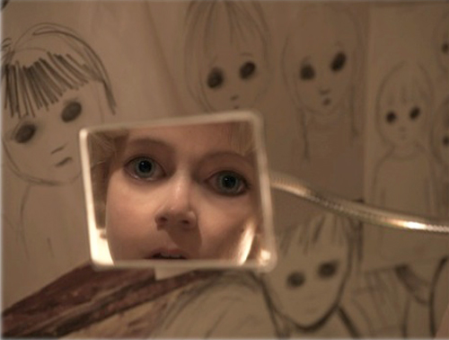 A child's eyes and face visible through a square cutout in a paper background covered in sketches of faces.