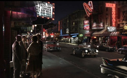 Nighttime city street with vintage cars, neon signs like Moulin Rouge, and people standing on a sidewalk.