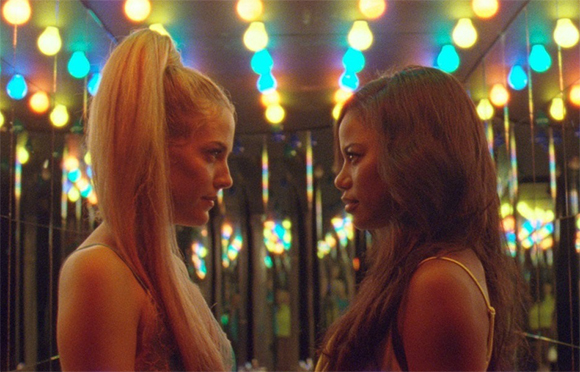 Two women in profile facing each other under a ceiling of glowing blue and yellow lights.