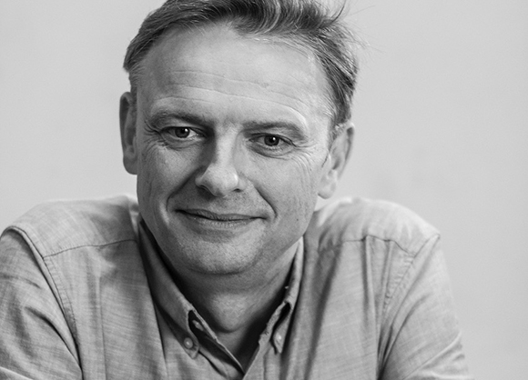 Black and white close-up portrait of a middle-aged man smiling at the camera.