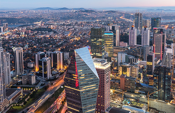 Aerial view of a dense metropolitan skyline with illuminated skyscrapers and winding roads at twilight.