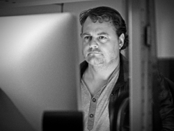 Black and white portrait of a man staring intently at a computer screen in a dimly lit room.