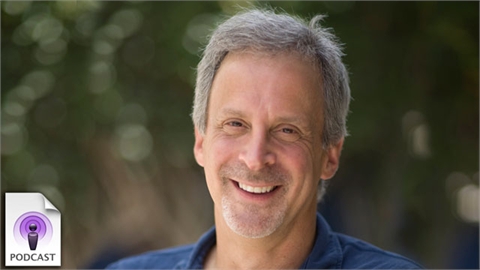 A smiling man with graying hair looking toward the camera against a blurred green background.