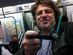 A man smiles while holding up a black multi-tool with several thin metal prongs and a blue antenna.