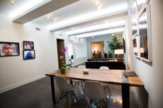 A bright, modern office space featuring a large wooden conference table and several grey chairs.