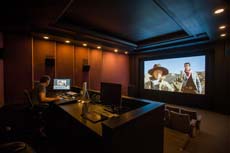A dark film editing studio featuring a large screen displaying a person and a computer workstation.
