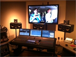A video editing suite with a large monitor showing a film scene, three computer screens, and studio speakers.
