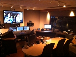 A dimly lit recording studio featuring a large screen, mixing consoles, and studio monitors.