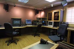 A production room with multiple computer monitors, workstations, black office chairs, and wooden cabinetry.