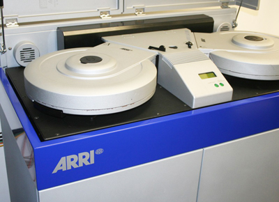A silver and blue ARRI film processing machine with two large circular drums and a control panel.
