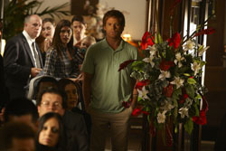 A man in a light green polo shirt stands in a crowded room next to a large bouquet of red and white flowers.