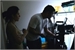 A woman and a man stand in silhouette working at a desk with computer equipment.