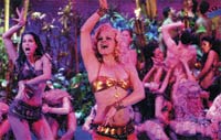 Several women in colorful, tropical-style dance costumes dancing under purple and blue lighting.