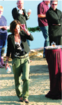 A woman in a black blazer and green trousers walks through an outdoor gathering.