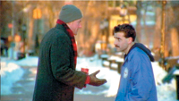 A man in a dark coat and beanie gestures toward a man in a blue jacket on a snowy path.