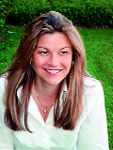 A woman with long brown hair smiling while wearing a white button-down shirt and a necklace.