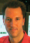 A man with dark hair wearing a red shirt looking toward the camera.