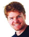 A smiling man with curly red hair and light-colored eyes looking toward the camera.
