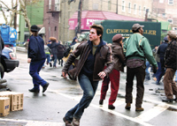 A man in a brown jacket and jeans runs through a busy city street filled with people and vehicles.
