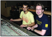 Two men standing behind a large audio mixing console in a studio setting.