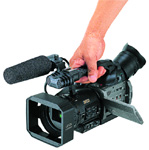 A person's hand gripping the handle of a black professional video camera with a microphone attached.
