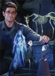 A man with glasses smiling next to various stop-motion animation character puppets.
