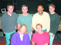 Six smiling people posing together in a music recording studio.