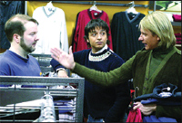 Three people engage in conversation near clothing racks in a retail store.