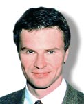 A man with dark hair wearing a grey suit jacket and a white shirt.
