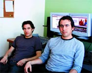 Two men sitting in an office in front of two computer monitors.