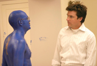 A man in a white striped shirt stares at a man whose entire body is covered in bright blue paint.