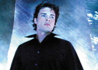 A man with dark hair wearing a black collared shirt looks upward against a blue textured background.