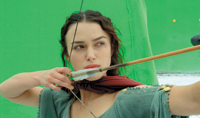 A woman with dark hair holds a bow and aims an arrow toward the camera against a green screen background.