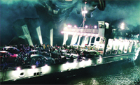 A ferry carrying several cars and many people travels through dark, misty water at night.